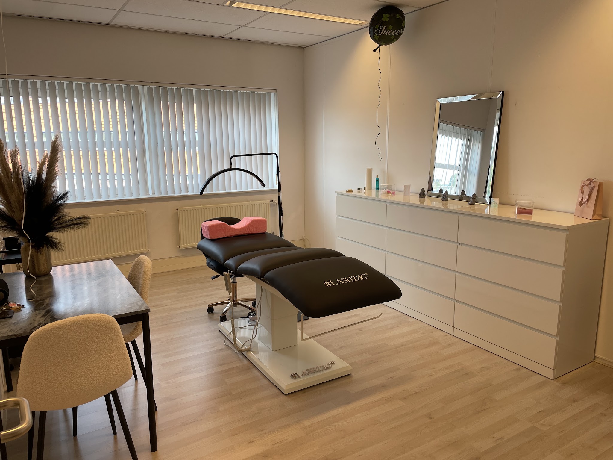 De studio: de behandelstoel, een tafel met stoelen, pampasgras en een grote spiegel boven de witte kast